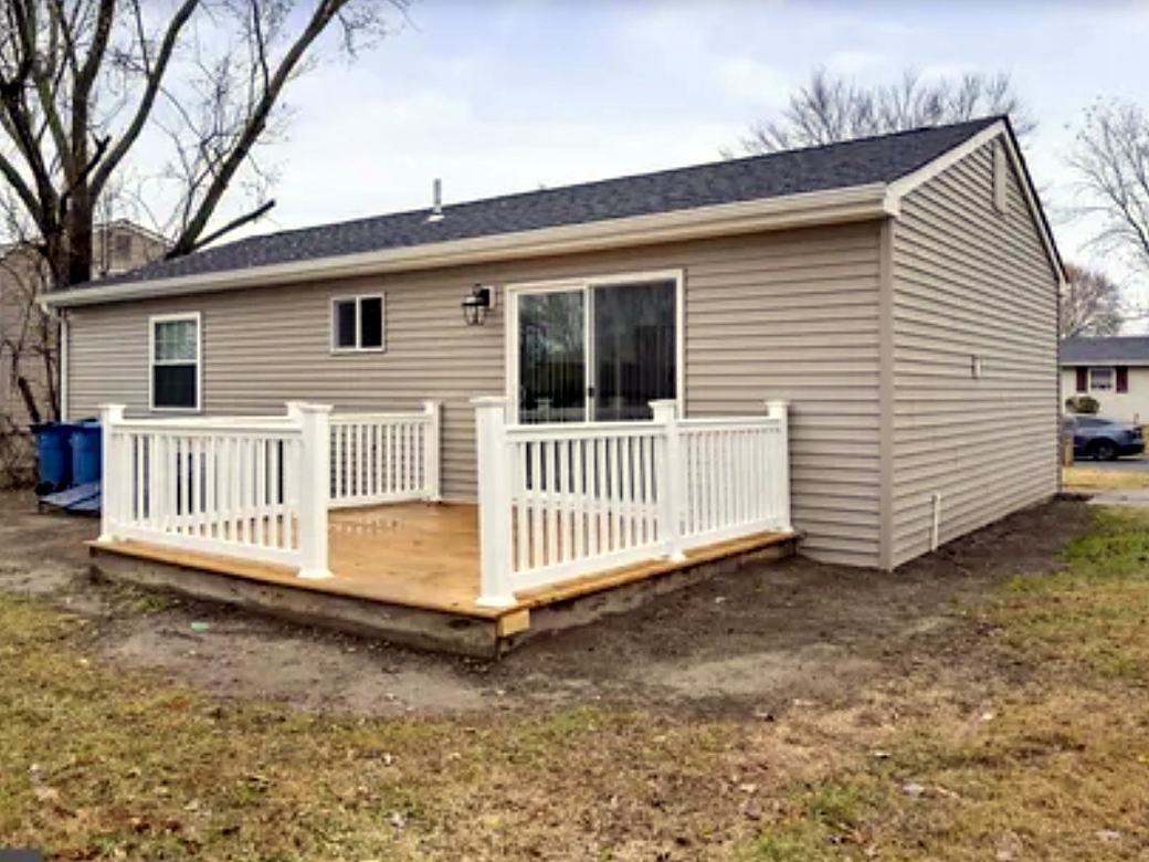 New wood deck with white vinyl railings on the back of a ranch home
