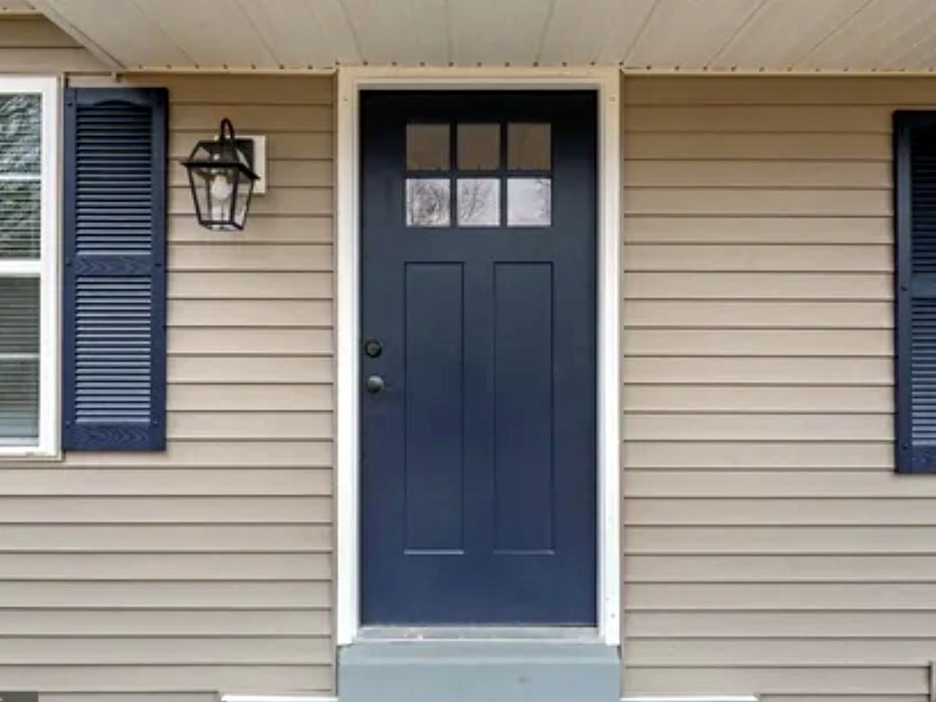 New navy front door and window with grilles set in beige siding