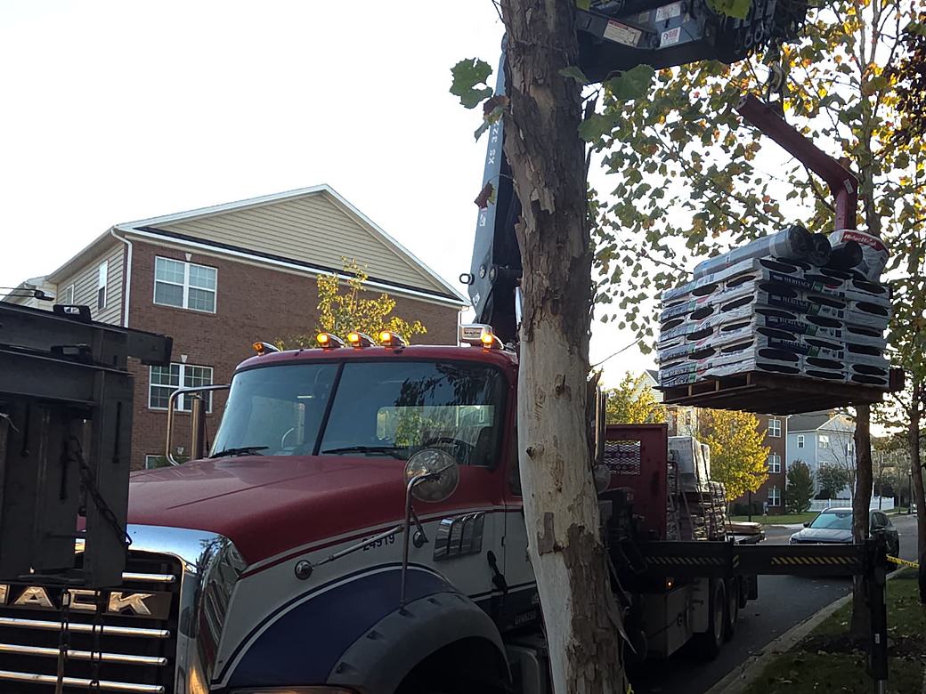 Boom truck lifting bundles of shingles onto a townhome roof