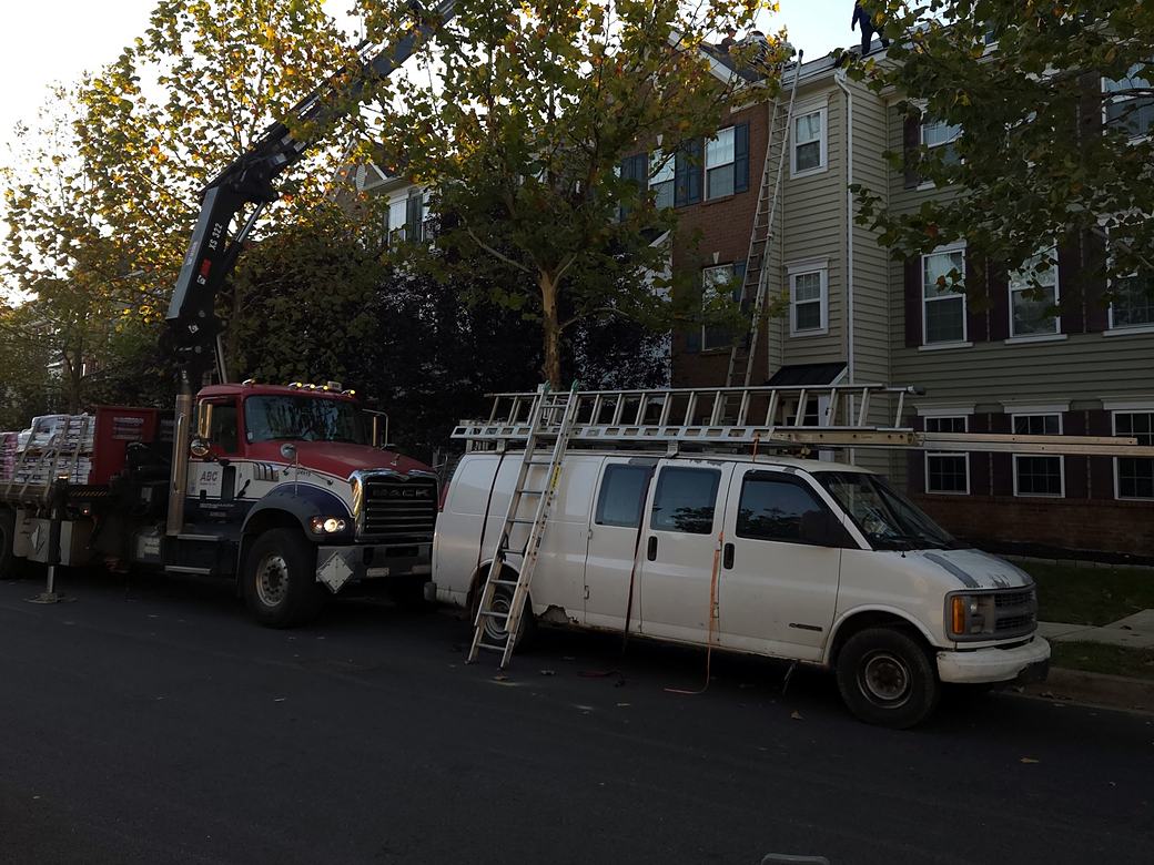 Work van and a boom truck delivering shingles to a townhome roofing job