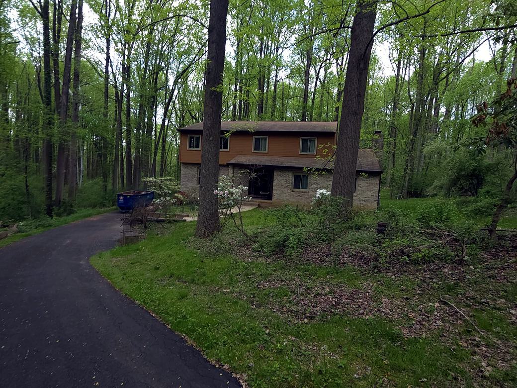 Two story home in the woods with brown siding seen from the driveway